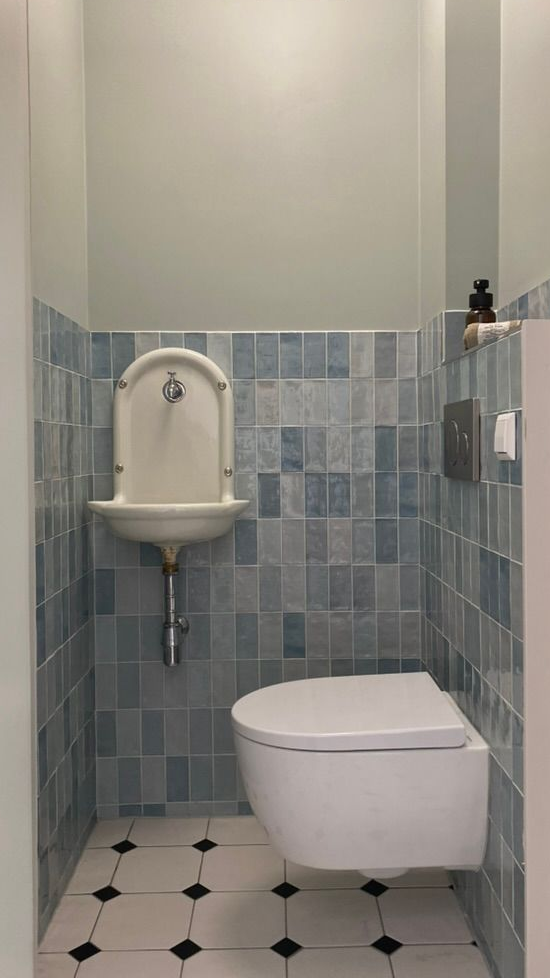 Kleine badkamer met blauwe tegelwanden, wandtoilet en antiek fonteintje zwart-witte vloertegels.