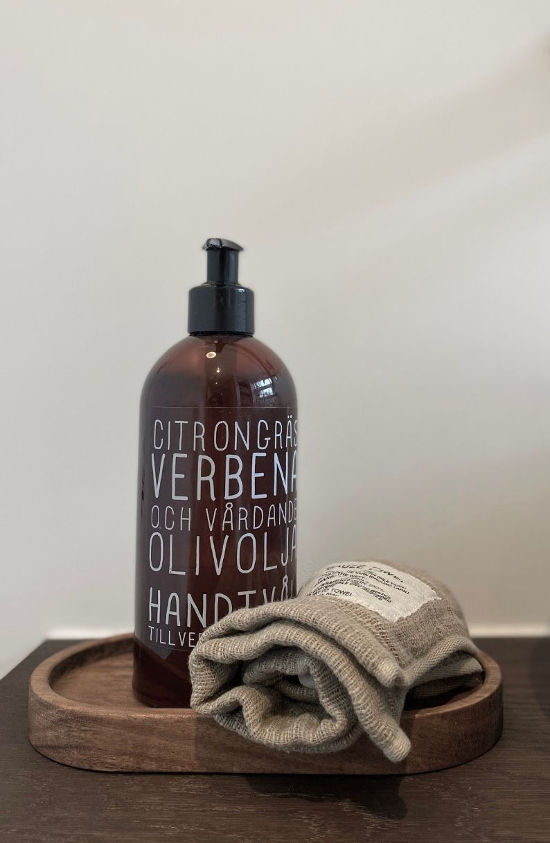 Een bruine fles zeep en een opgevouwen handdoekje op een houten dienblad.