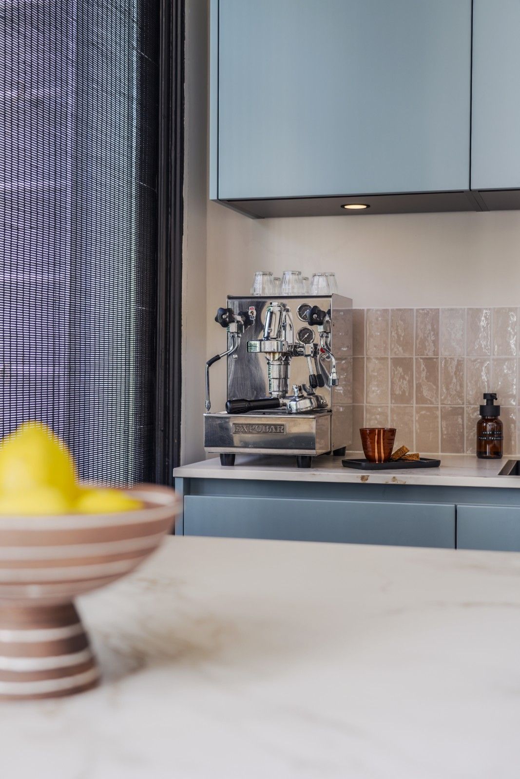 Espressomachine op een aanrecht met blauwe kastjes en een tegel achterwand