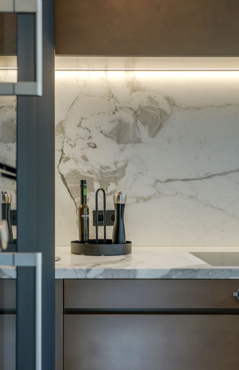 Keukenblad met marmeren achterwand, verlicht door een ledstrip, met olijfolie, pepermolen en zoutvaatje.