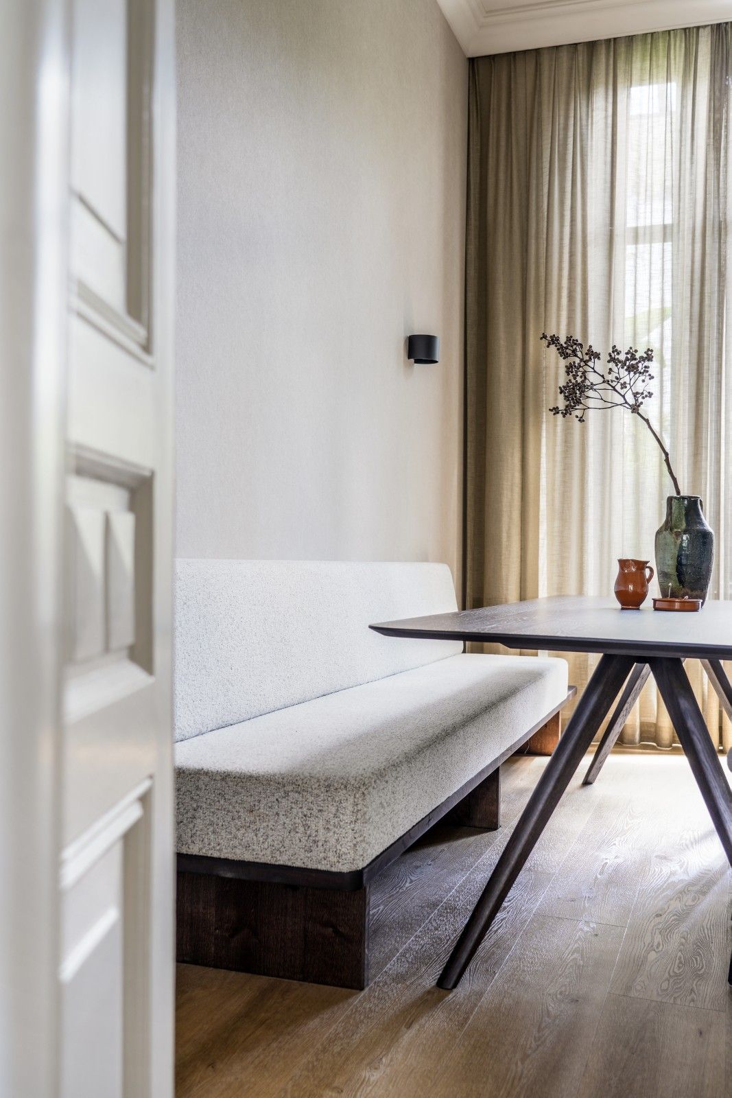 Eethoek met een gestoffeerde bank met structuur, een donkere eettafel en transparante gordijnen.