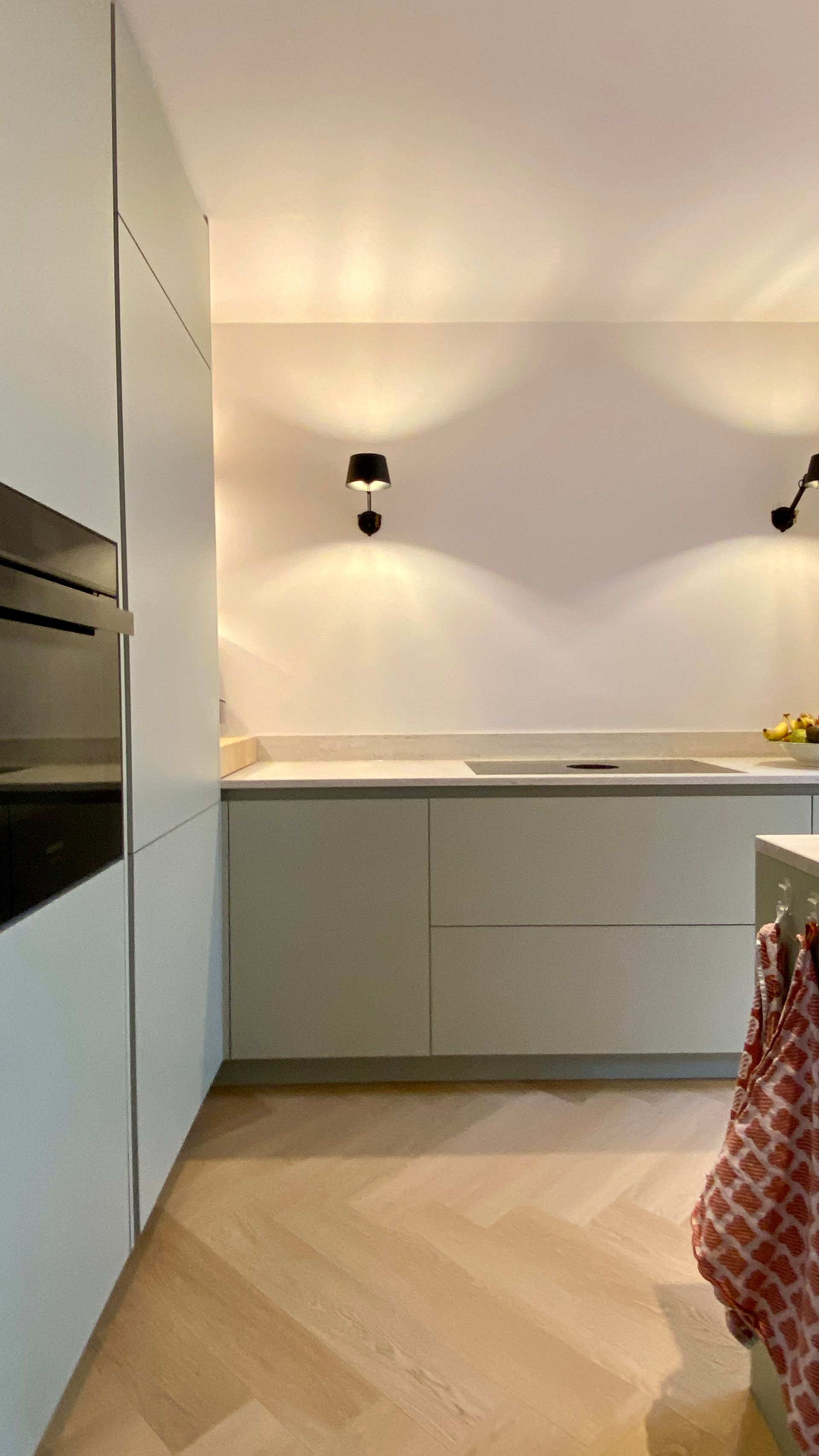 Moderne keuken met lichtgroene kasten, lichte houten vloer en zwarte wandlampen.