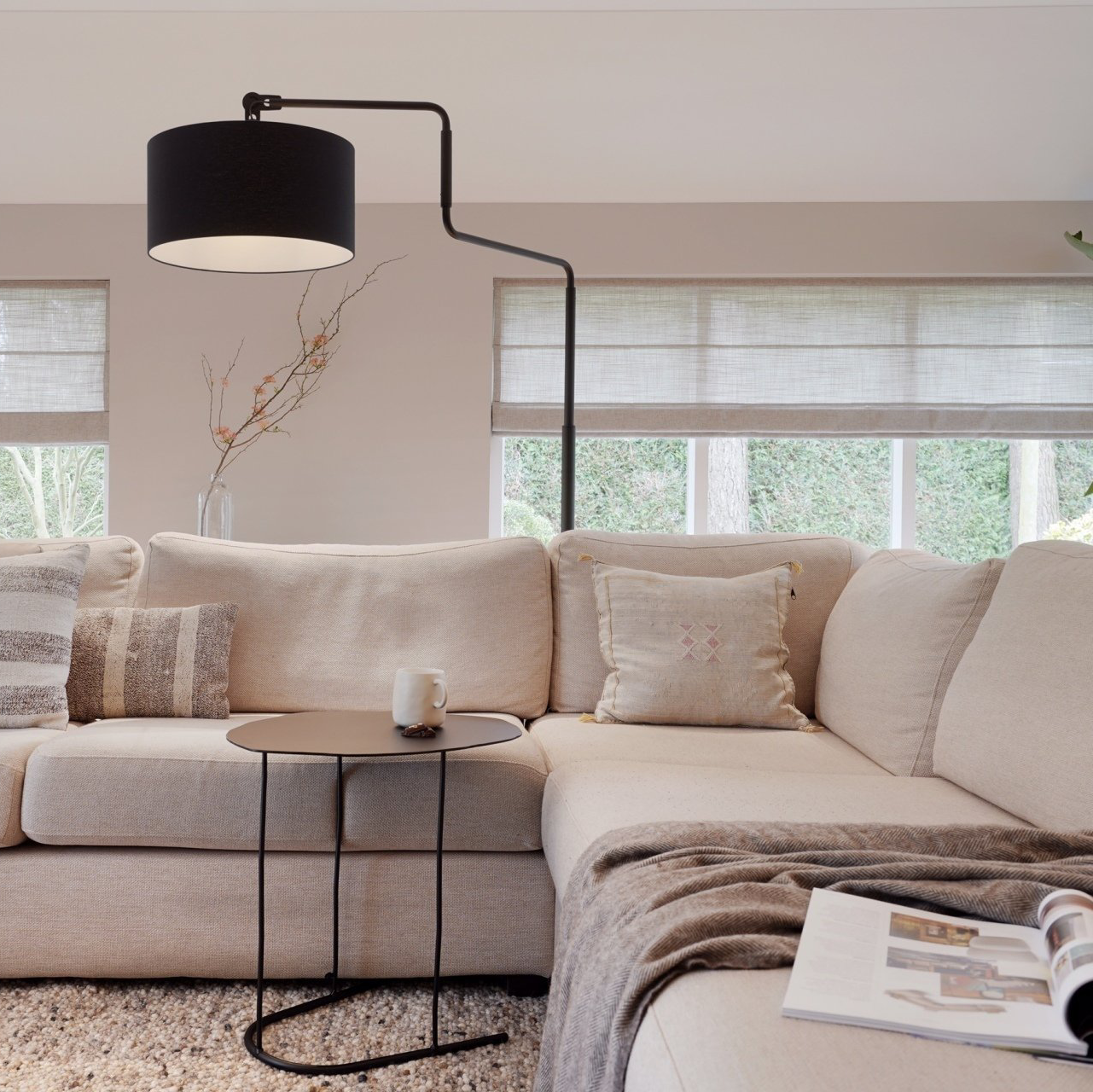 Woonkamer met een zwarte lamp, beige hoekbank en een bijzettafel | Villa18 Interieurs