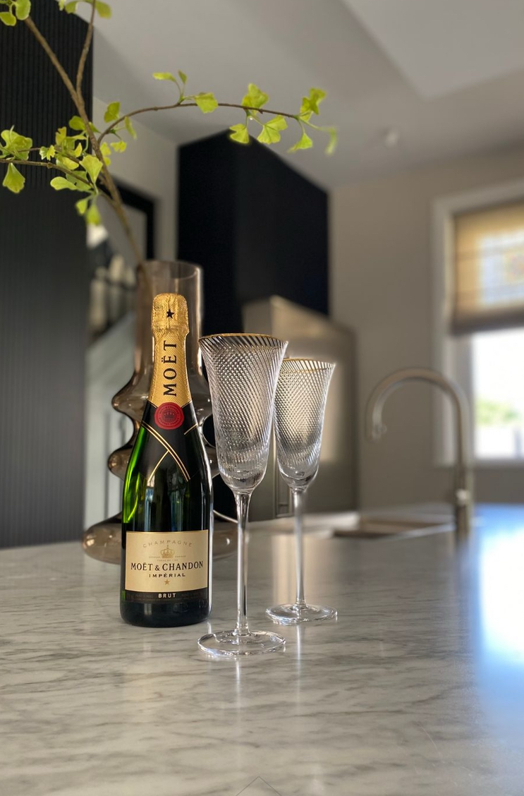 Een fles Moët-champagne en twee flutes op een marmeren aanrecht met een groene tak.