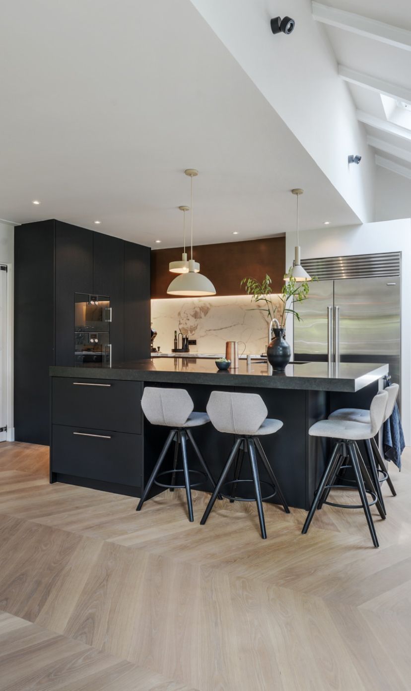 Moderne zwarte keuken met kookeiland en lichte houten visgraat vloer. Grijze draaibare krukken bij het kookeiland.