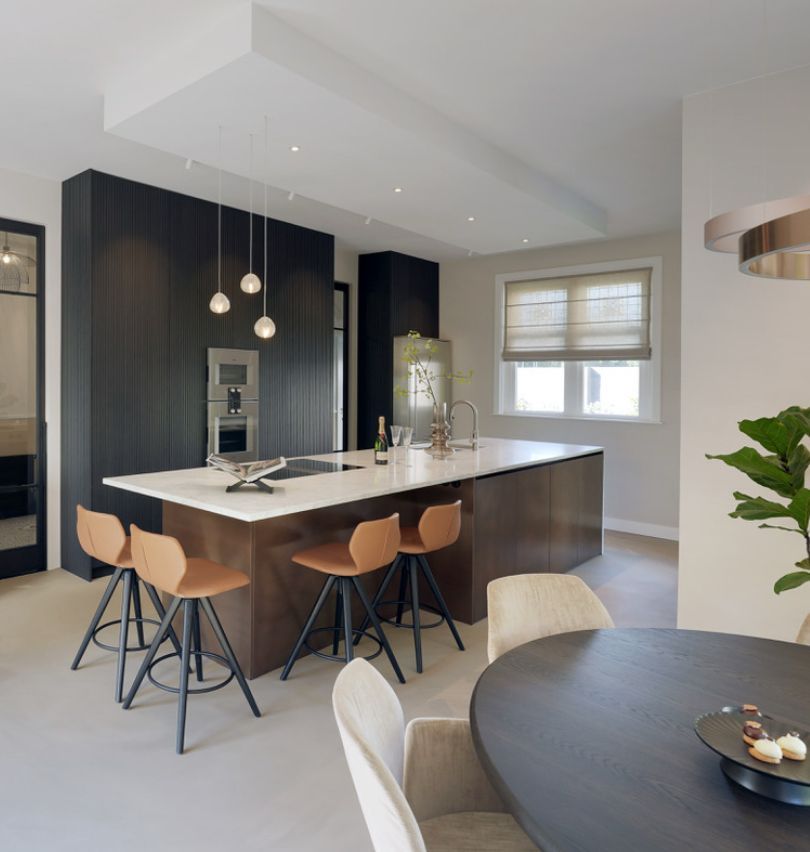Luxe leefkeuken met kookeiland en leren barkrukken. Verlichting kookeiland