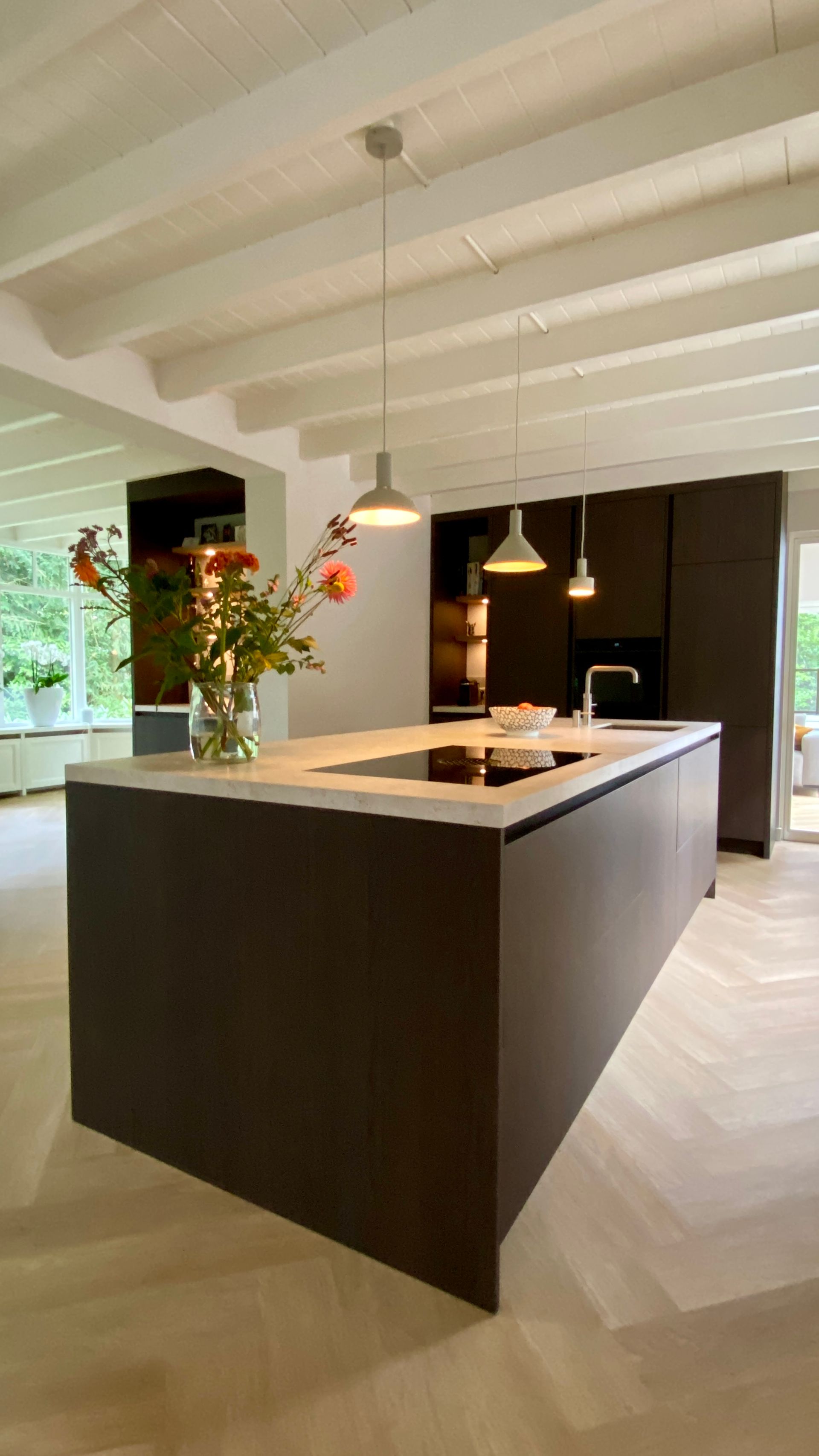 Moderne keuken met donkere kasten, lichte aanrechtbladen en houten vloeren. Het kookeiland is voorzien van een spoelbak en hanglampen.