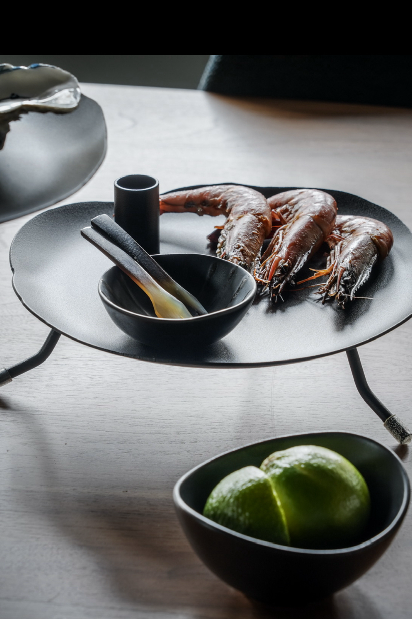 Bord met garnalen, kom met tang, limoenen en kleine kommen op tafel.