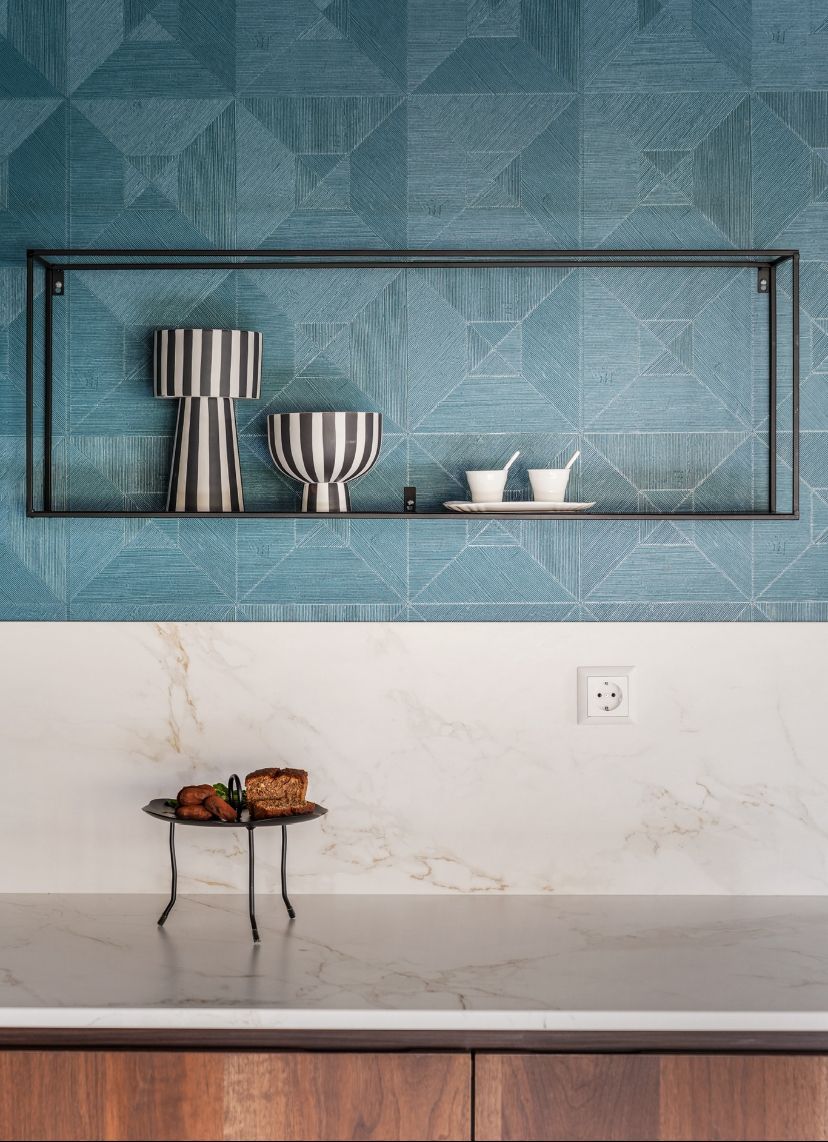 Keuken met een blauw Arte behang met grafisch patroon, wit marmer aanrechtblad en decoratieve plank.