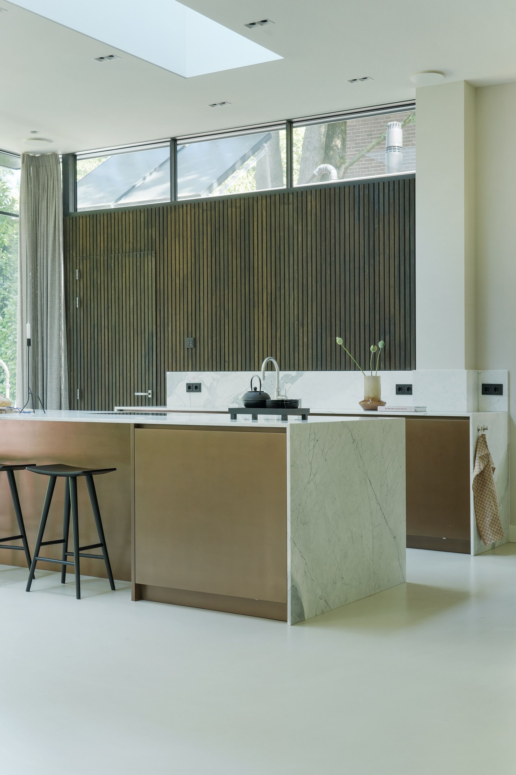 Moderne keuken met bronzen kasten, witte marmeren aanrechtbladen en houten latten wand.