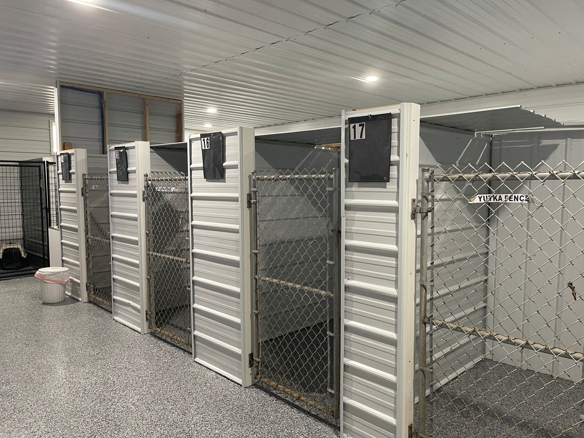 Indoor dog kennels in a row, with wire doors and gray walls. Shiny floor and ceiling.