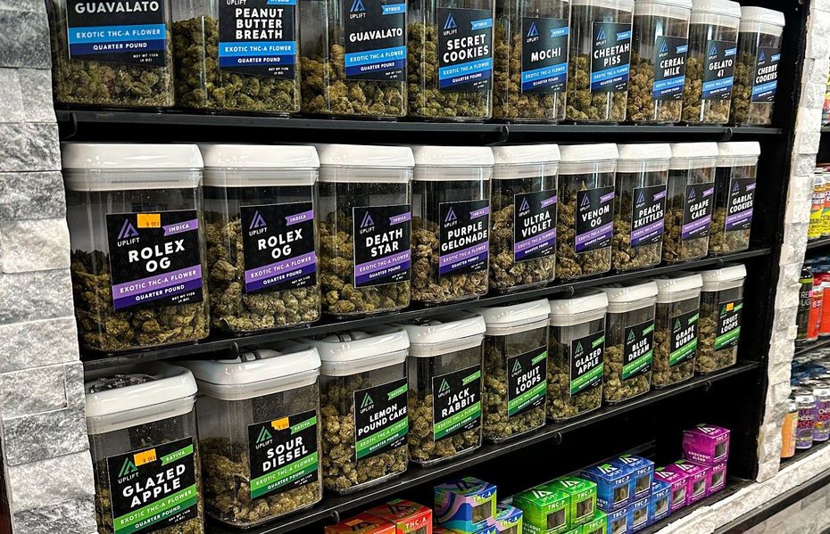 Shelves filled with various clear jars containing dried cannabis flower in a retail store setting.