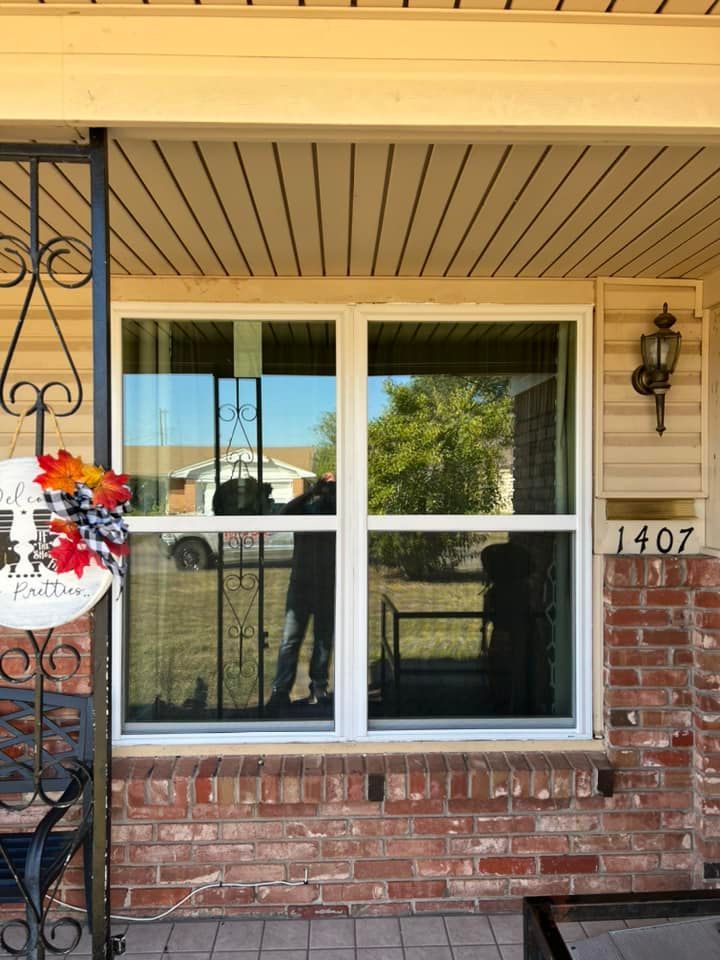 A brick house with a white window and a wreath on the porch.