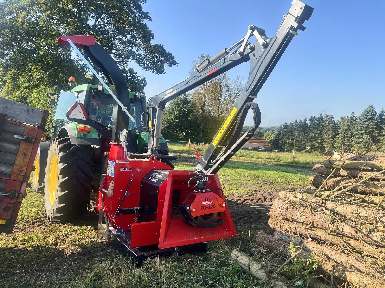 A wood chipper with a forest grapple mounted on a crane is ready to chip a pile of logs.