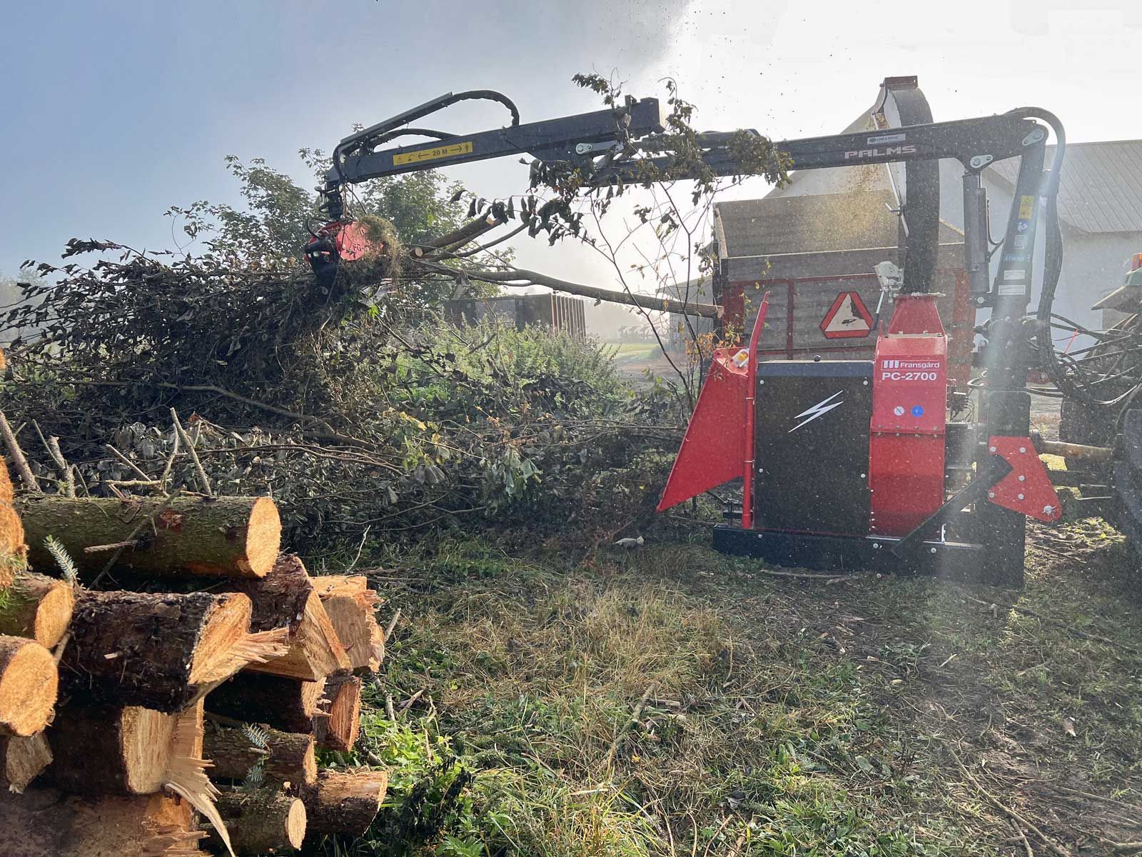 A Wood chipper is cutting a pile of logs in a field.