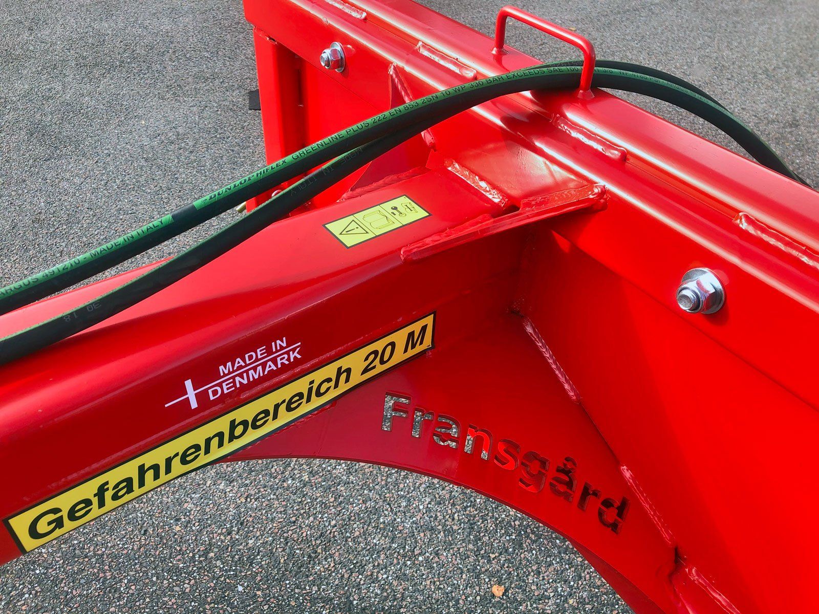 Et nærbillede af en rød skovtang med en hydraulikslange fastgjort til den.