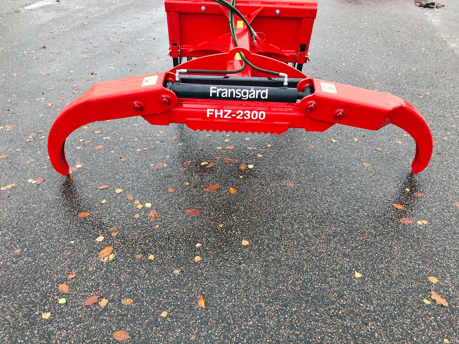 En rød hydraulisk griber står på jorden.