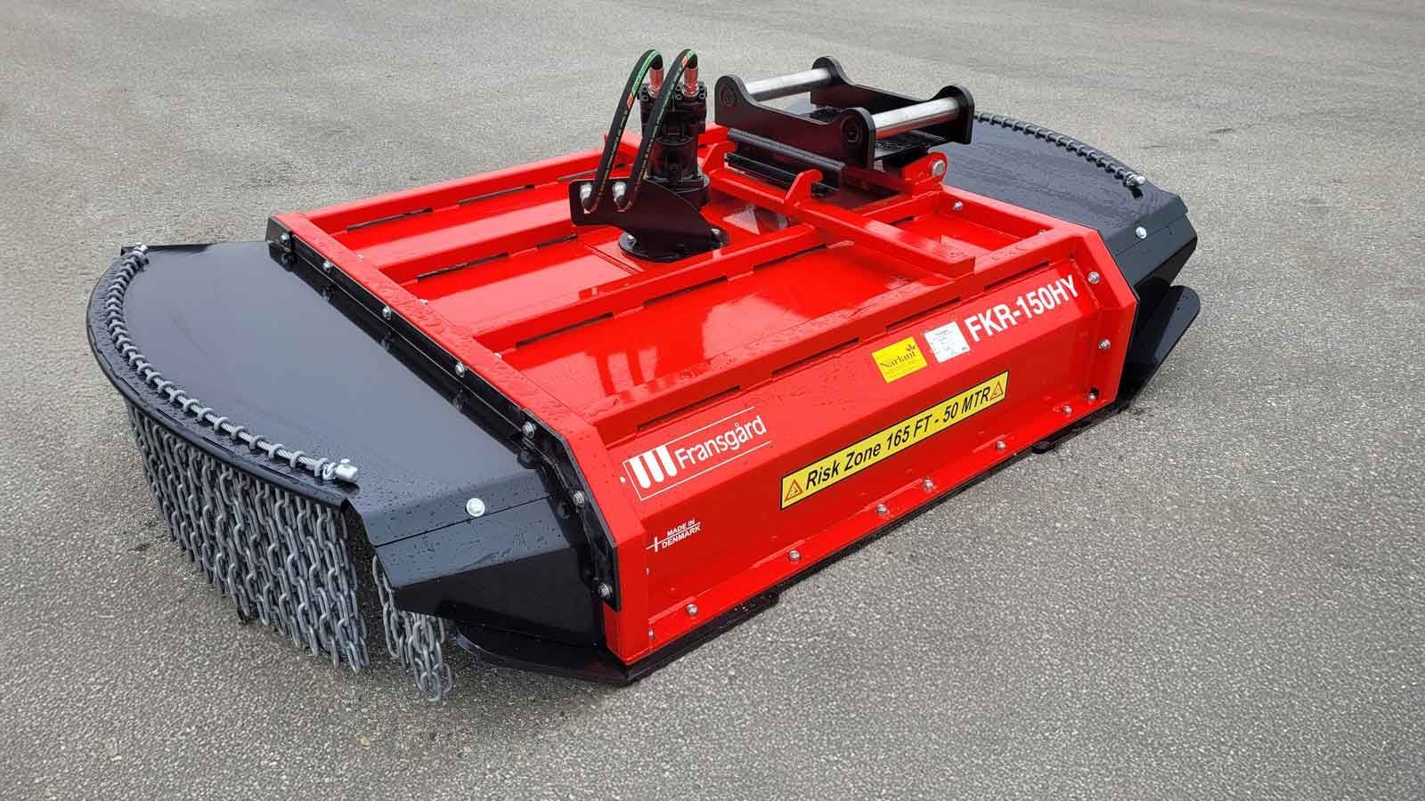En blå traktor med en kæderydder bagpå kører gennem en frodig grøn skov