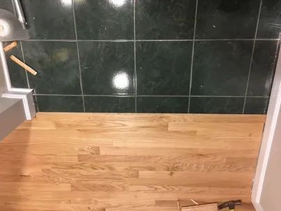 Empty room with light wood floor and dark tiled wall, with a small tool on the floor