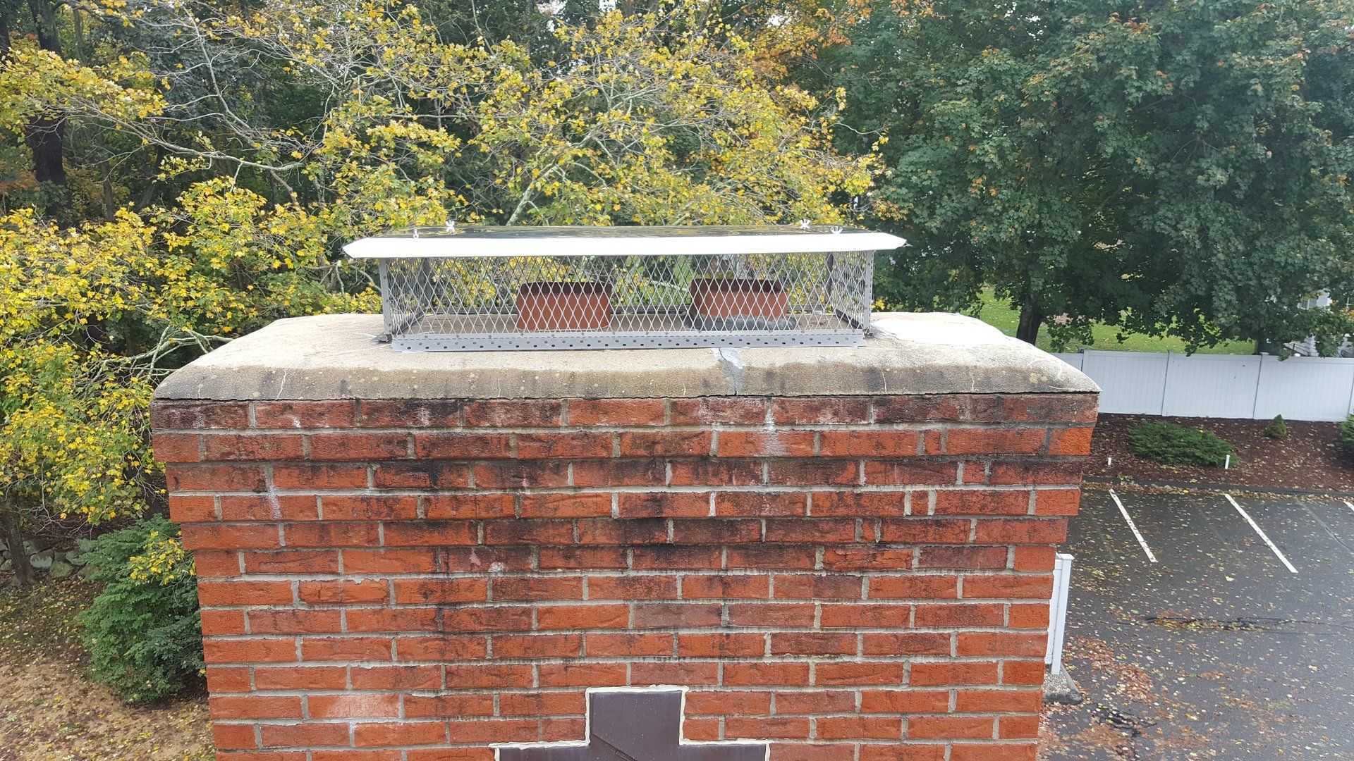 A brick chimney with a cross on it is in a parking lot.