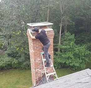 A man is standing on a ladder on top of a brick chimney.