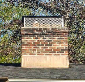 A brick chimney on top of a roof with trees in the background.