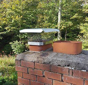 A chimney on top of a brick wall with trees in the background.