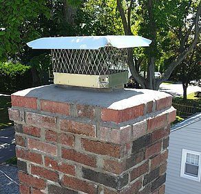 A brick chimney with a metal cover on top of it.