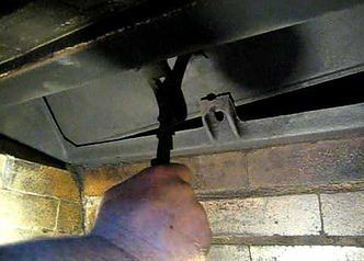 A person is holding a hose under a car in a garage.