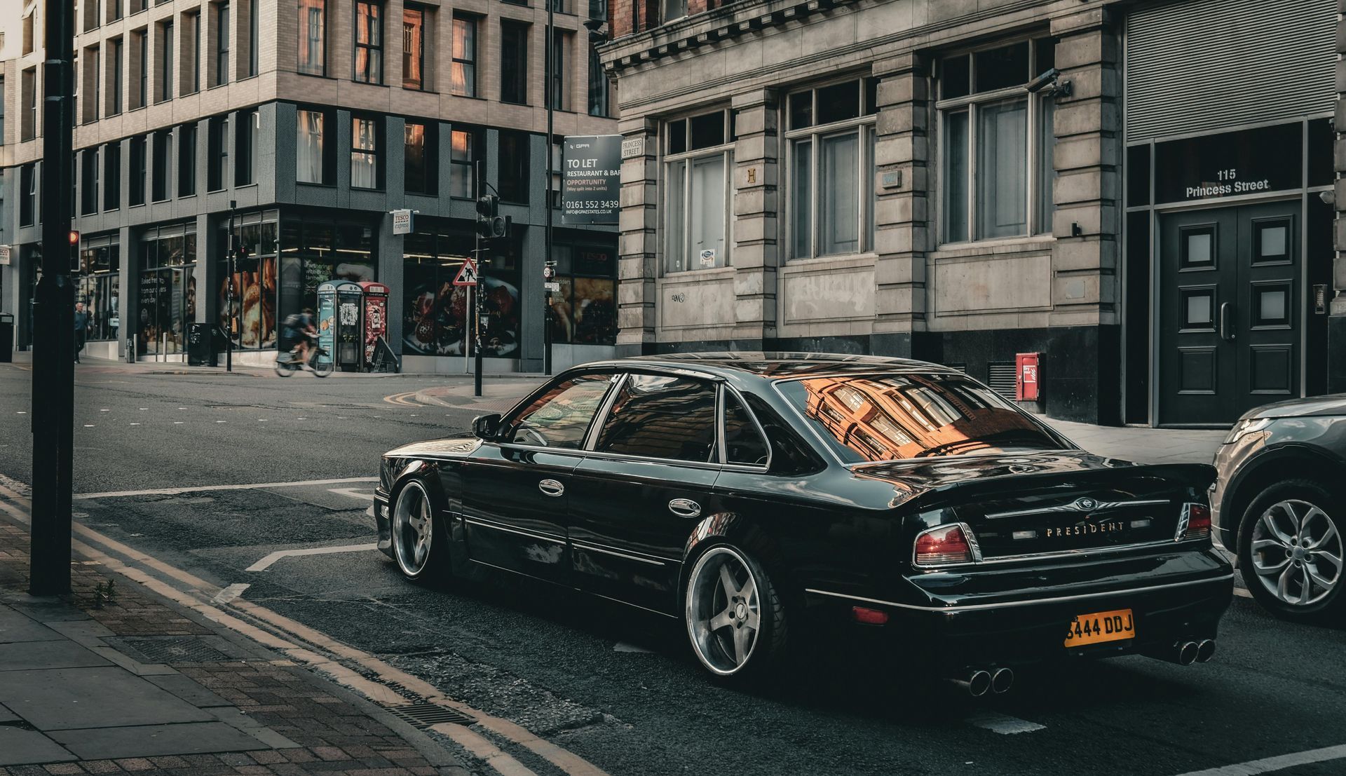 A black car is parked on the side of the road in front of a building.