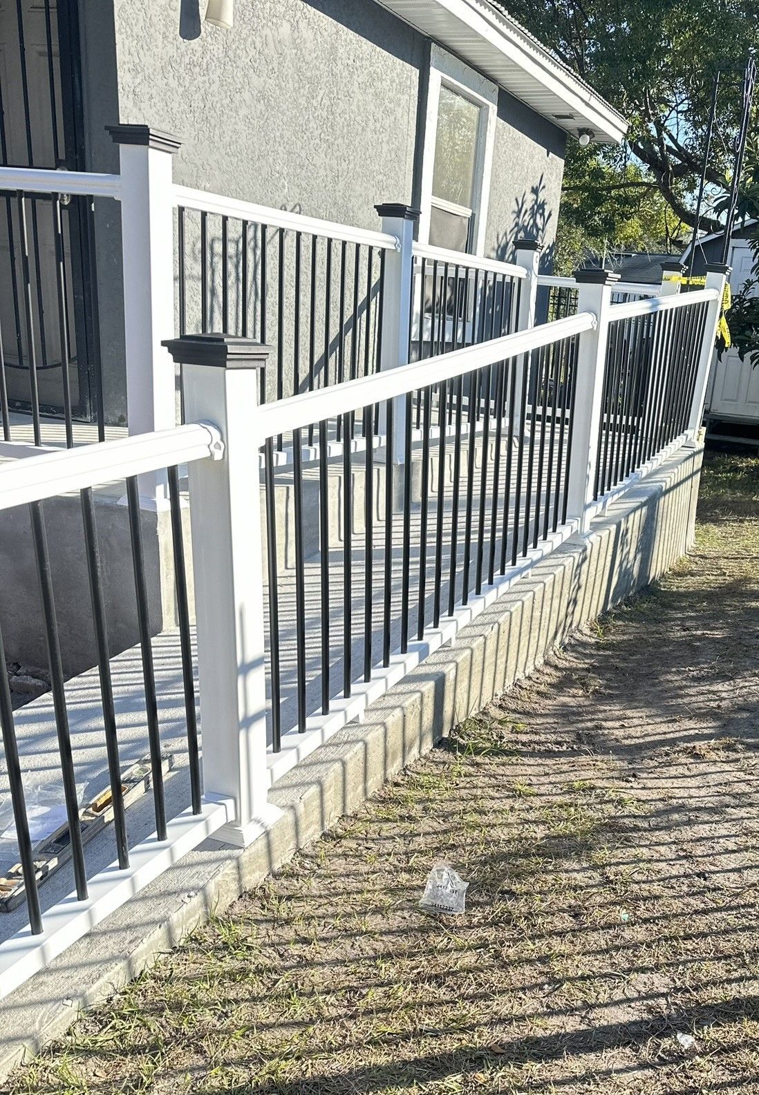 A white fence with black railings is on a concrete porch and ramp.