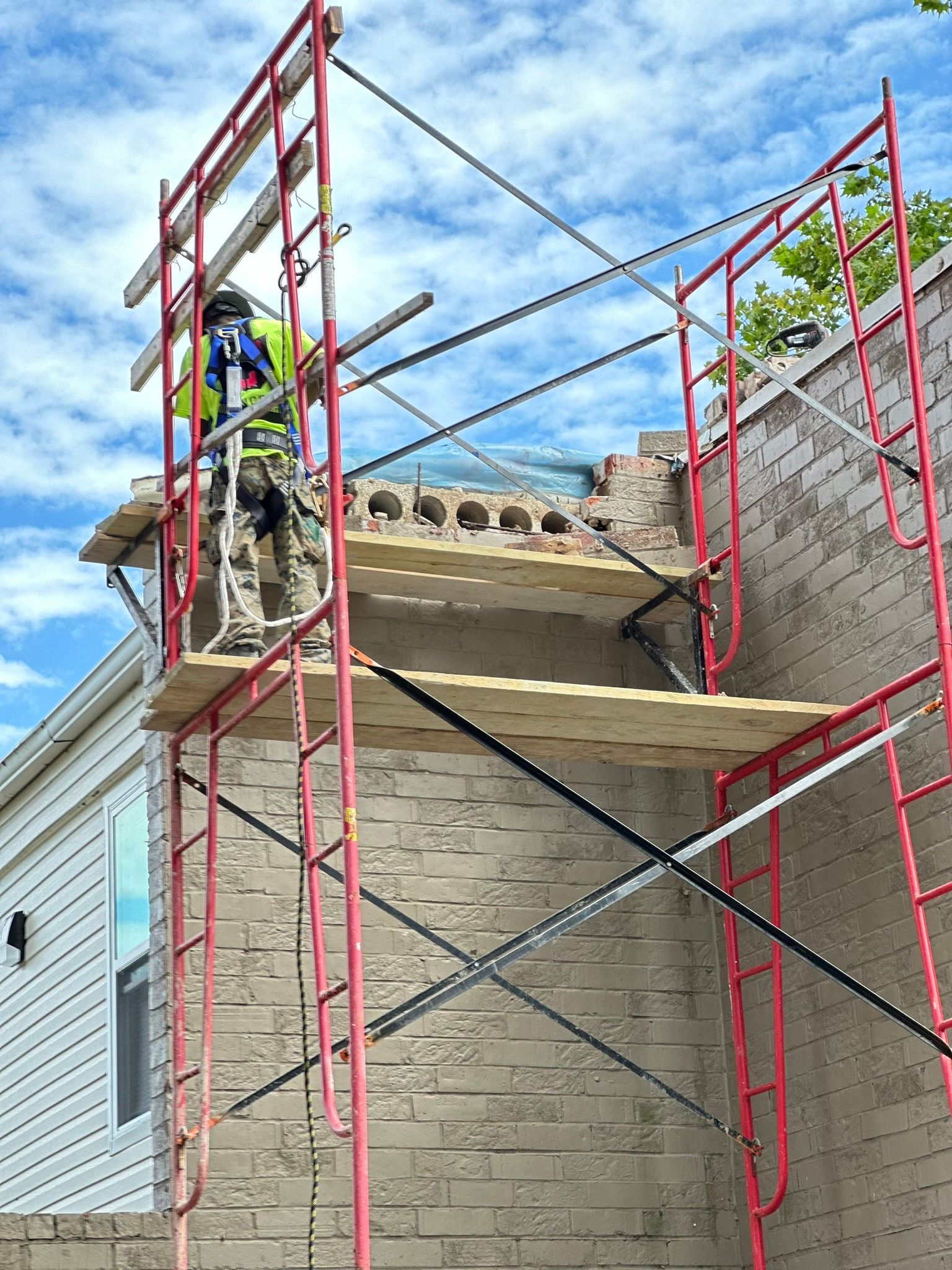A man is standing on top of a red scaffolding doing masonry repairs.