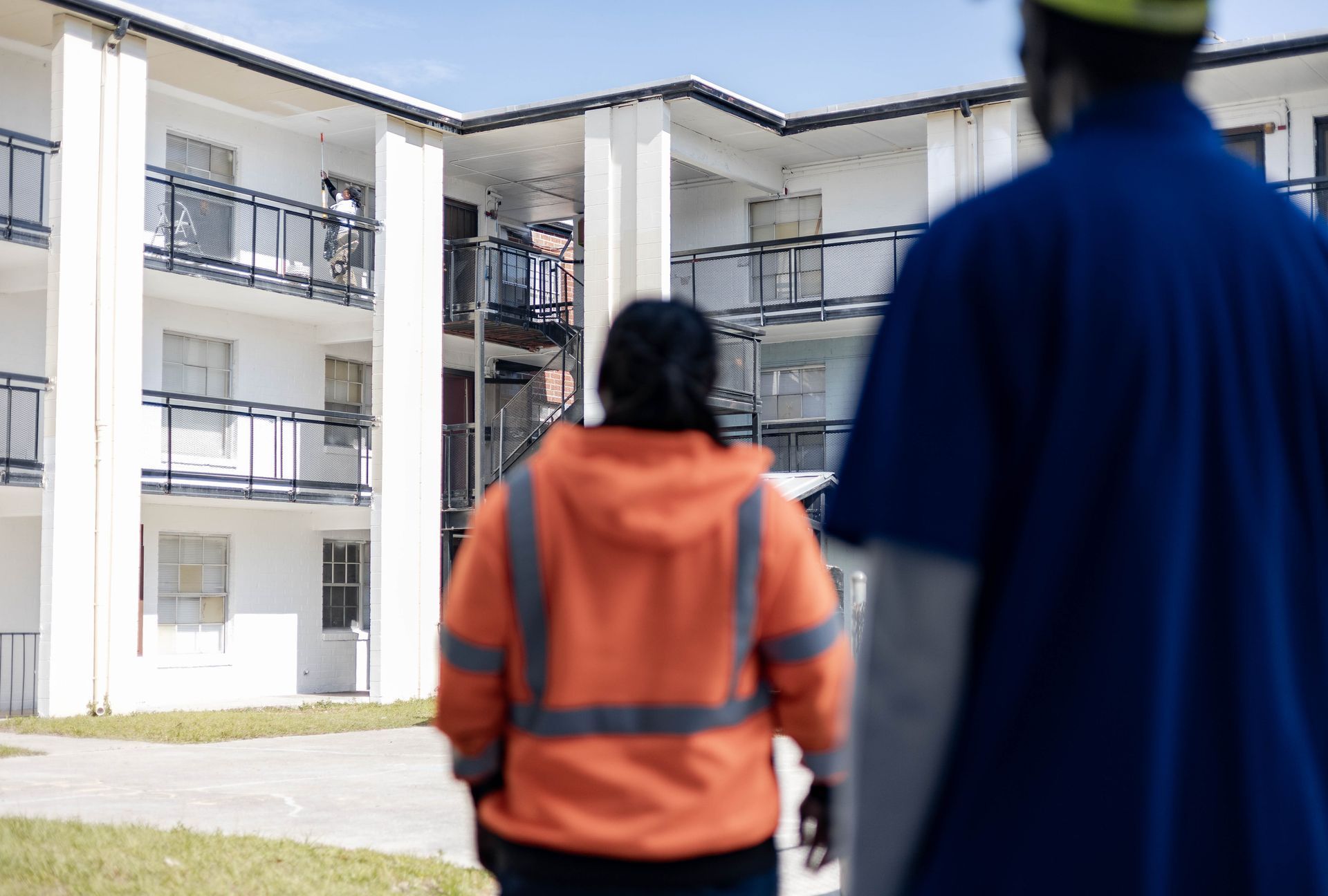 two men are watching a woman painting a building.