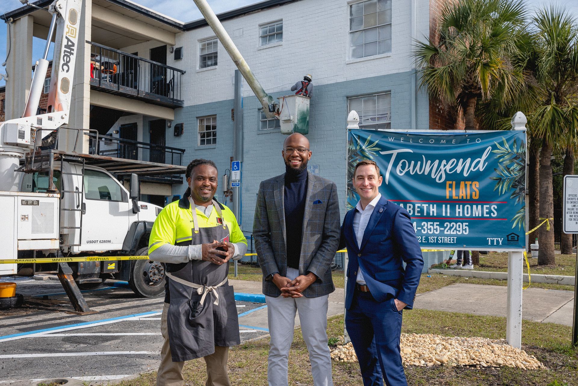 Three men are standing in front of a building next to a sign.