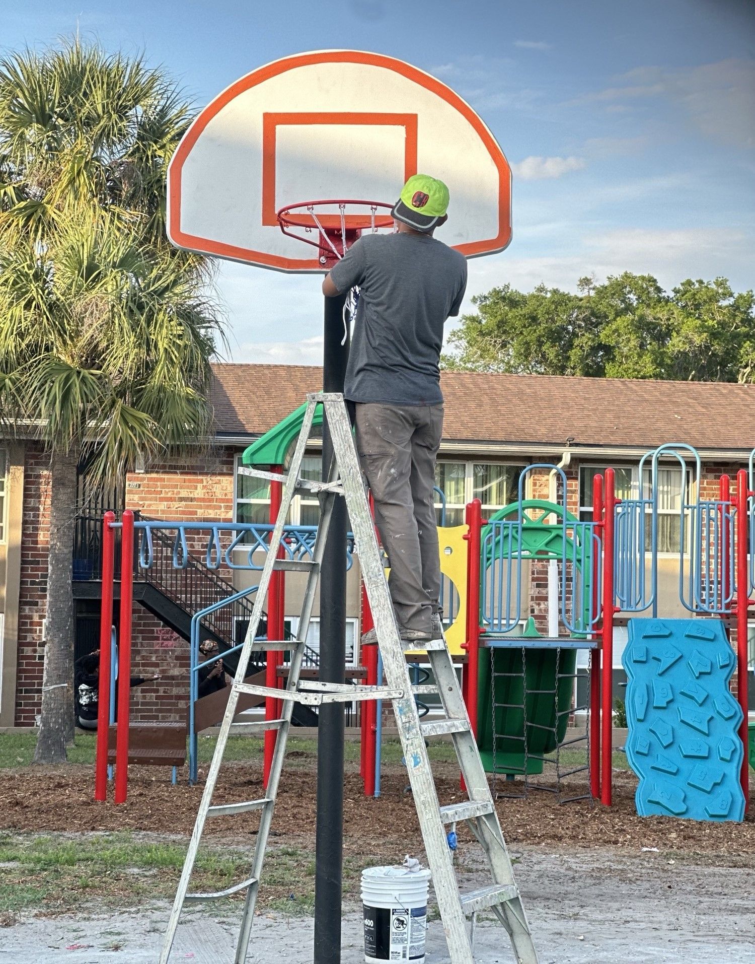 A man is standing on a ladder installing a basketball hoop.