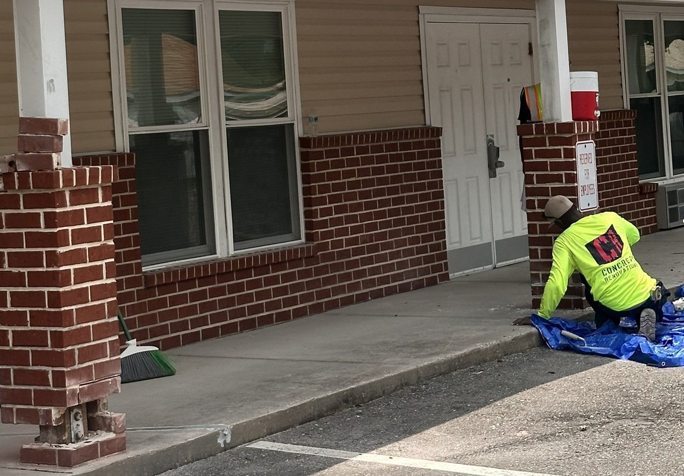 A man is kneeling on the sidewalk in front of a brick building.