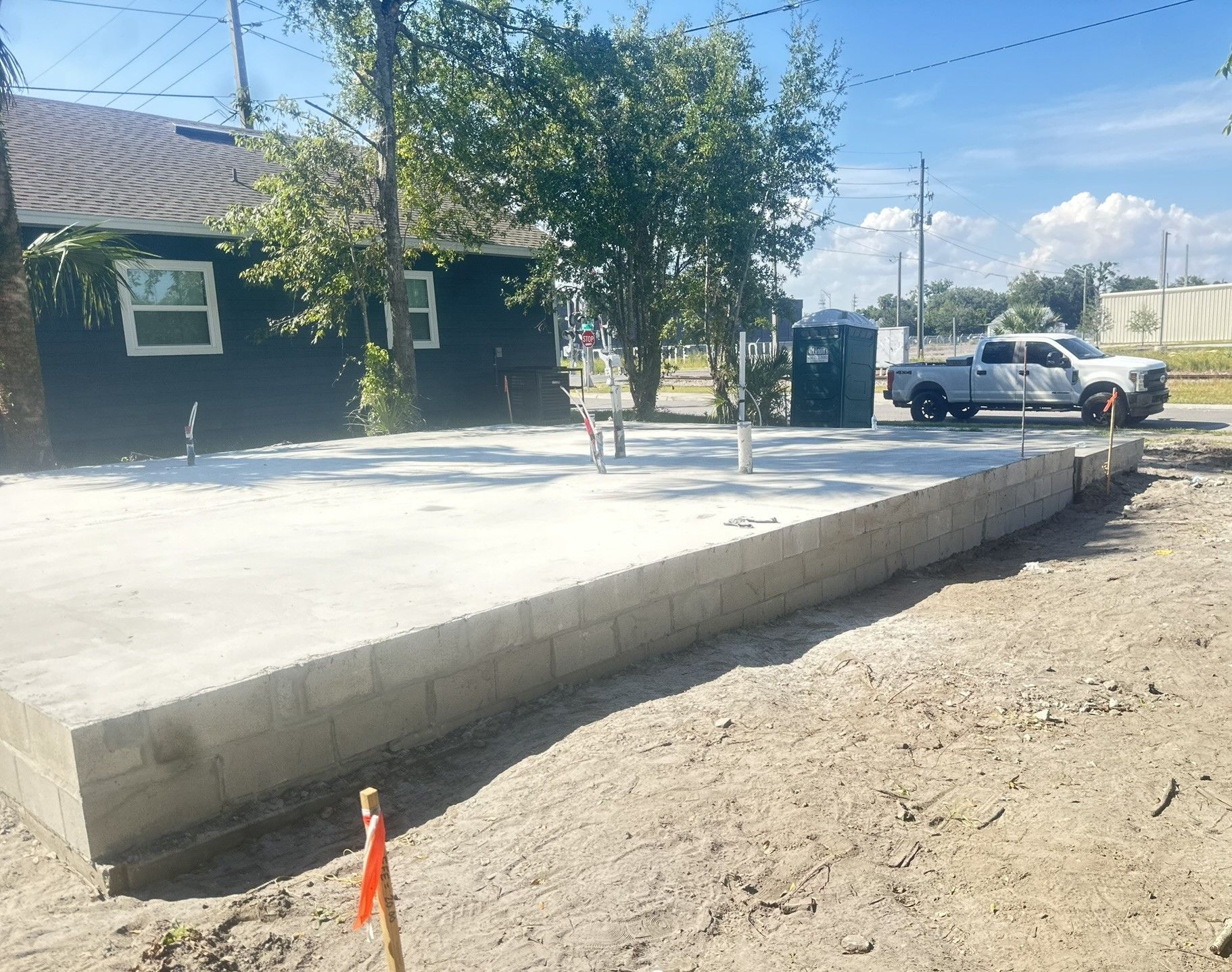 Concrete foundation with cinder block wall, construction site. White pickup truck and porta potty visible.