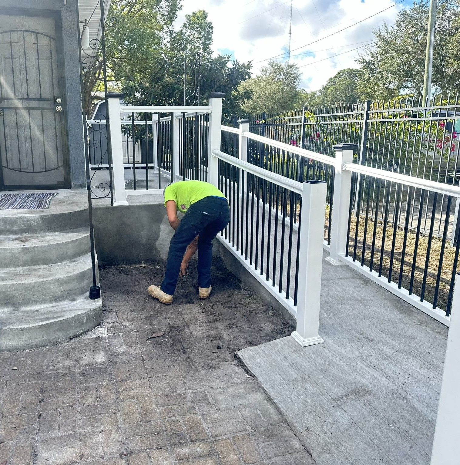 A man in a yellow shirt is kneeling down in front of a white railing.