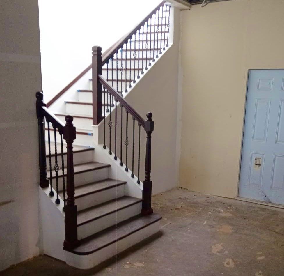 Staircase with dark wood railing and white steps in an unfinished room. Light blue door visible.