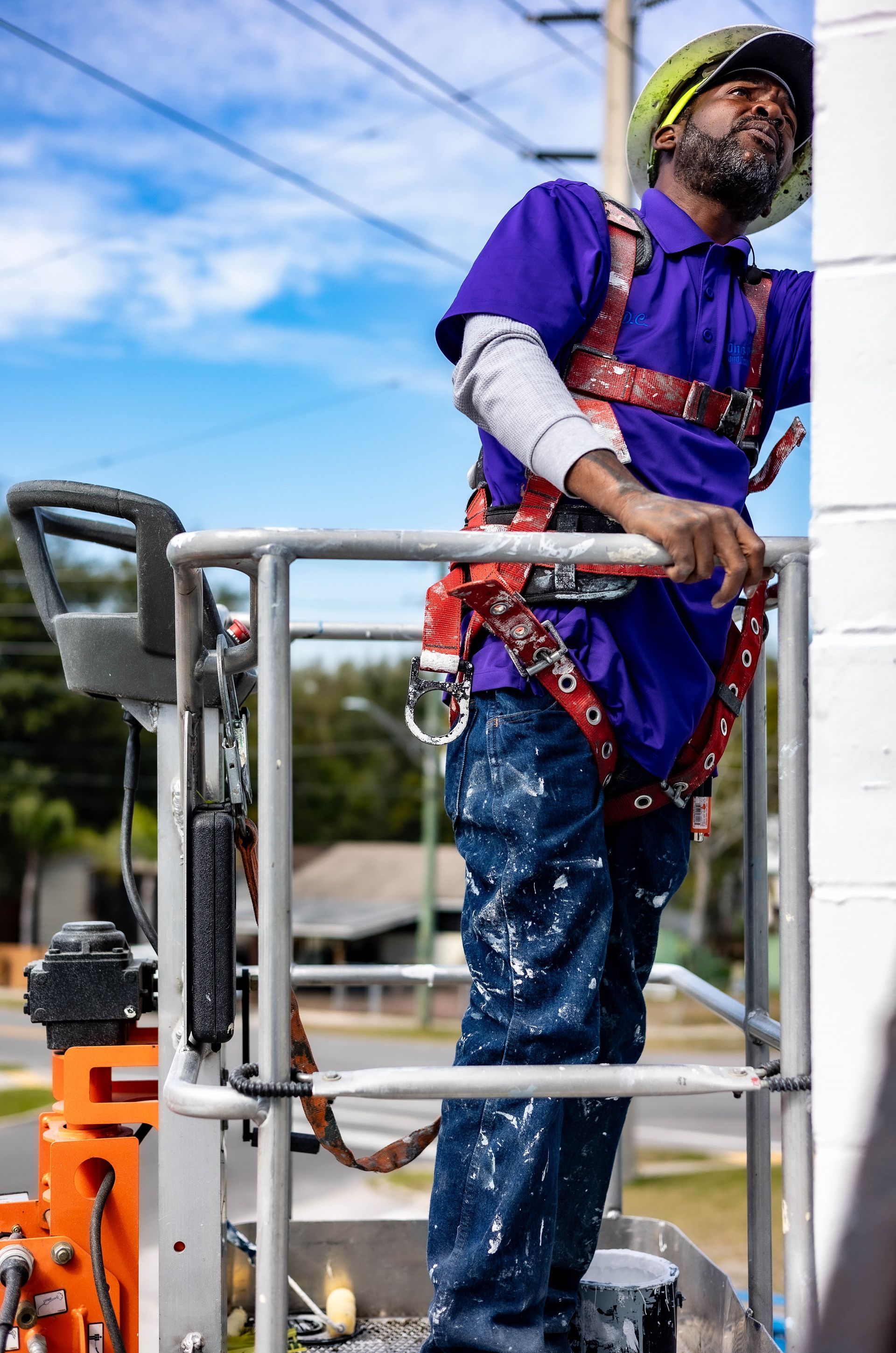 A man in a purple shirt is standing on a ladder painting a wall.