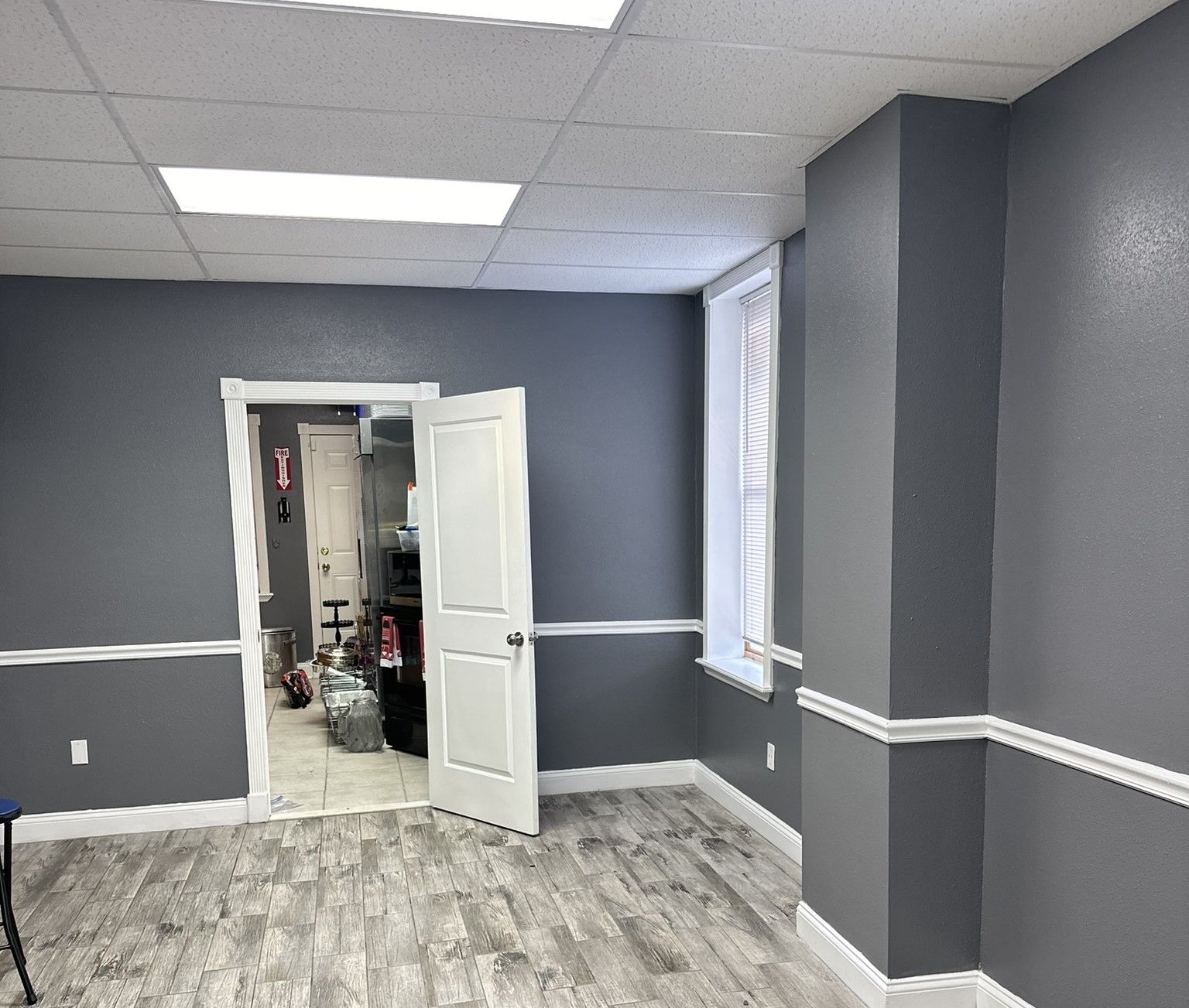 Empty room with grey walls, white trim, and a door leading to another room. White door slightly ajar.