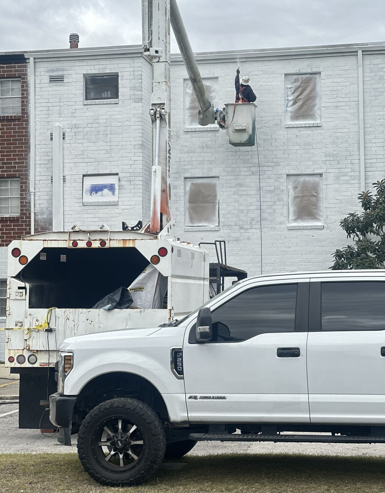 A white truck is parked in front of a man painting a brick building .