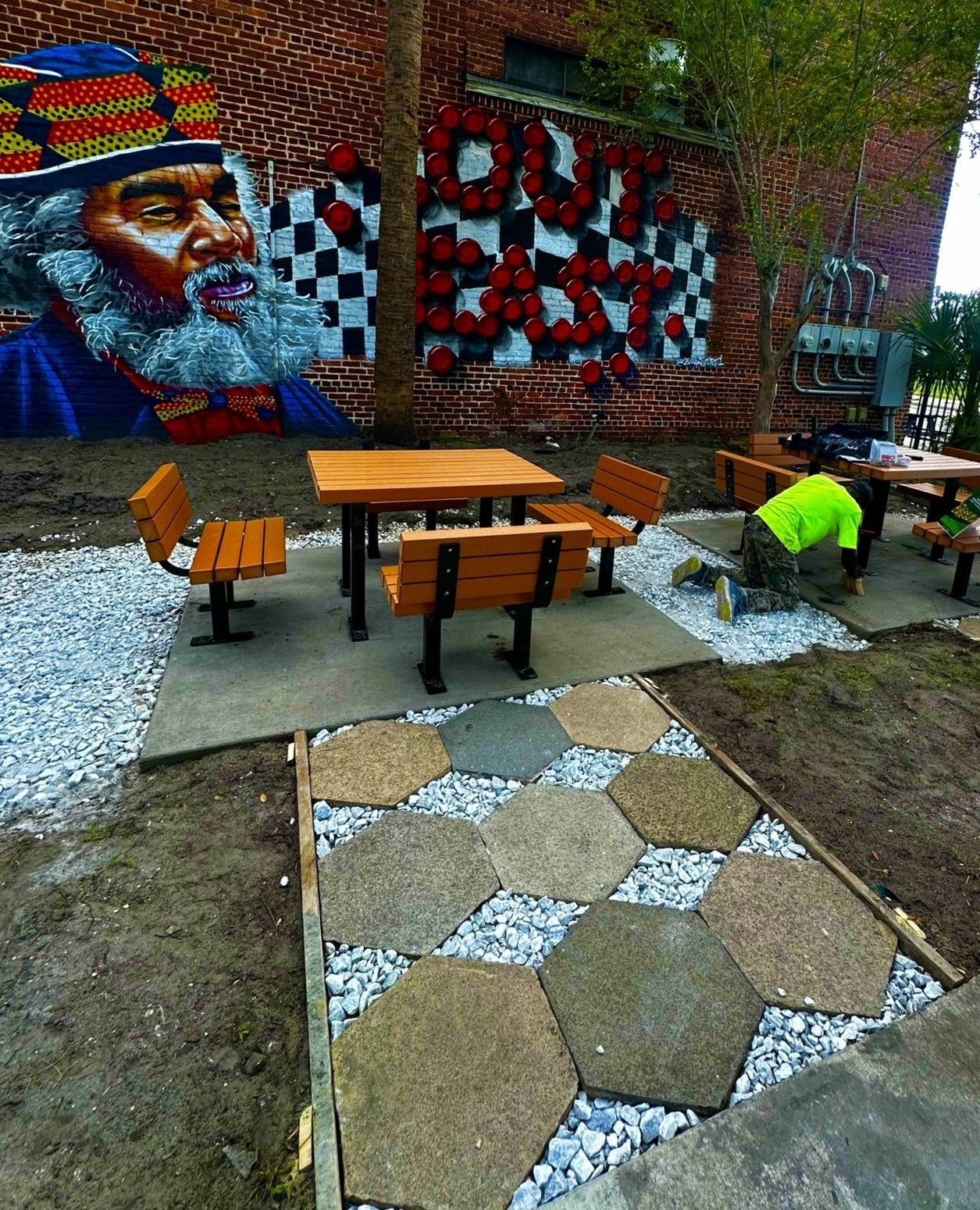 A man is installing a paver in front of a brick wall with graffiti on it.