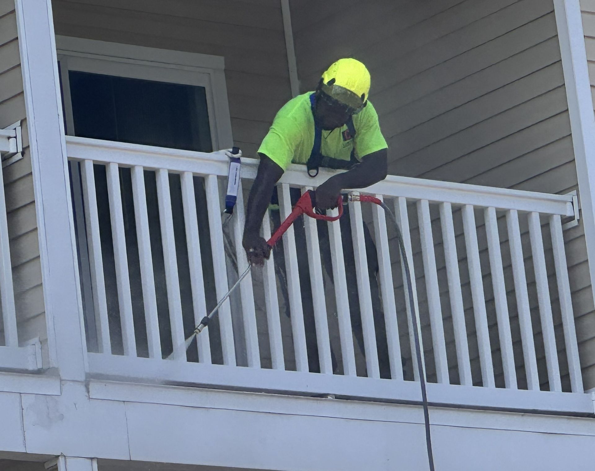 A man is cleaning a balcony railing with a high pressure washer.