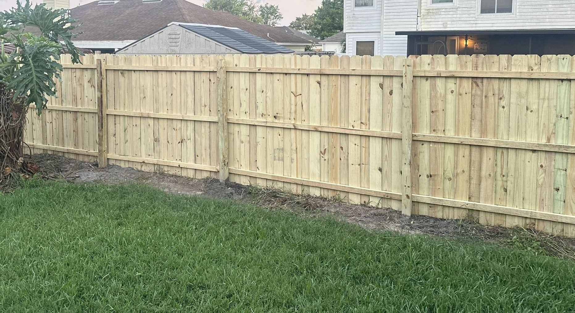 A wooden fence surrounds a patio with chairs and a table.