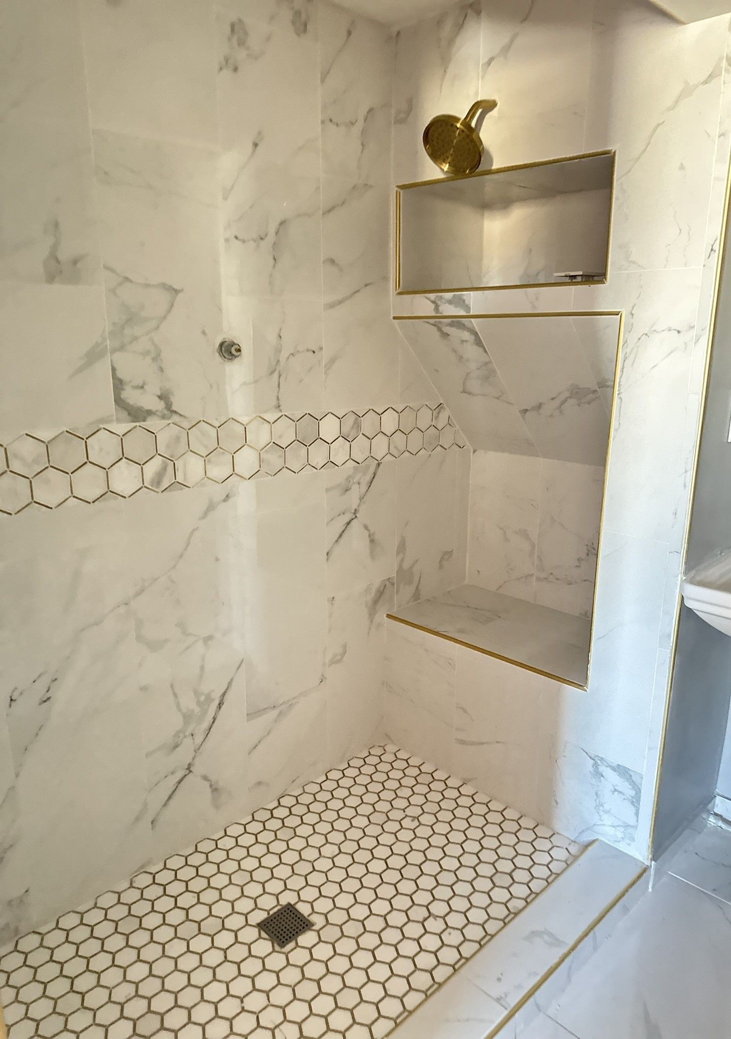 Marble-tiled shower with a pebble floor and built-in shelves. Gold trim accents and decorative tile band.