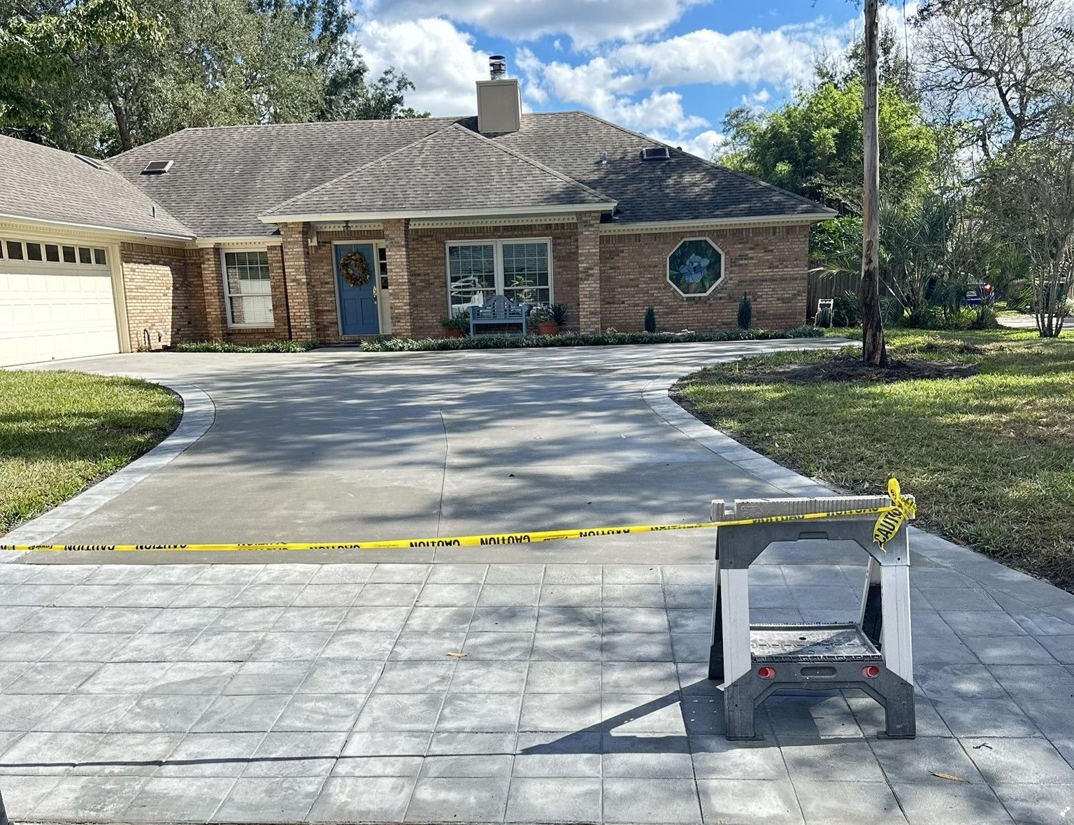 Home with gray brick exterior, driveway under construction with caution tape.