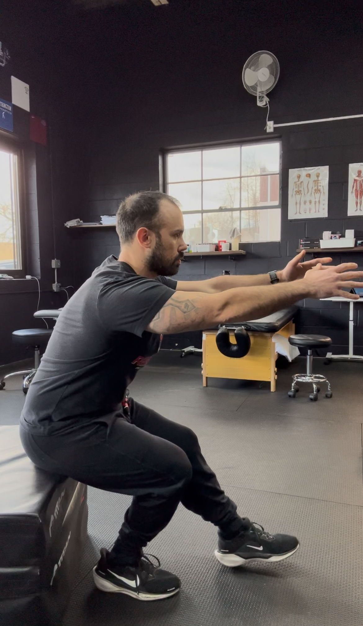 A man is squatting on a box in a gym.
