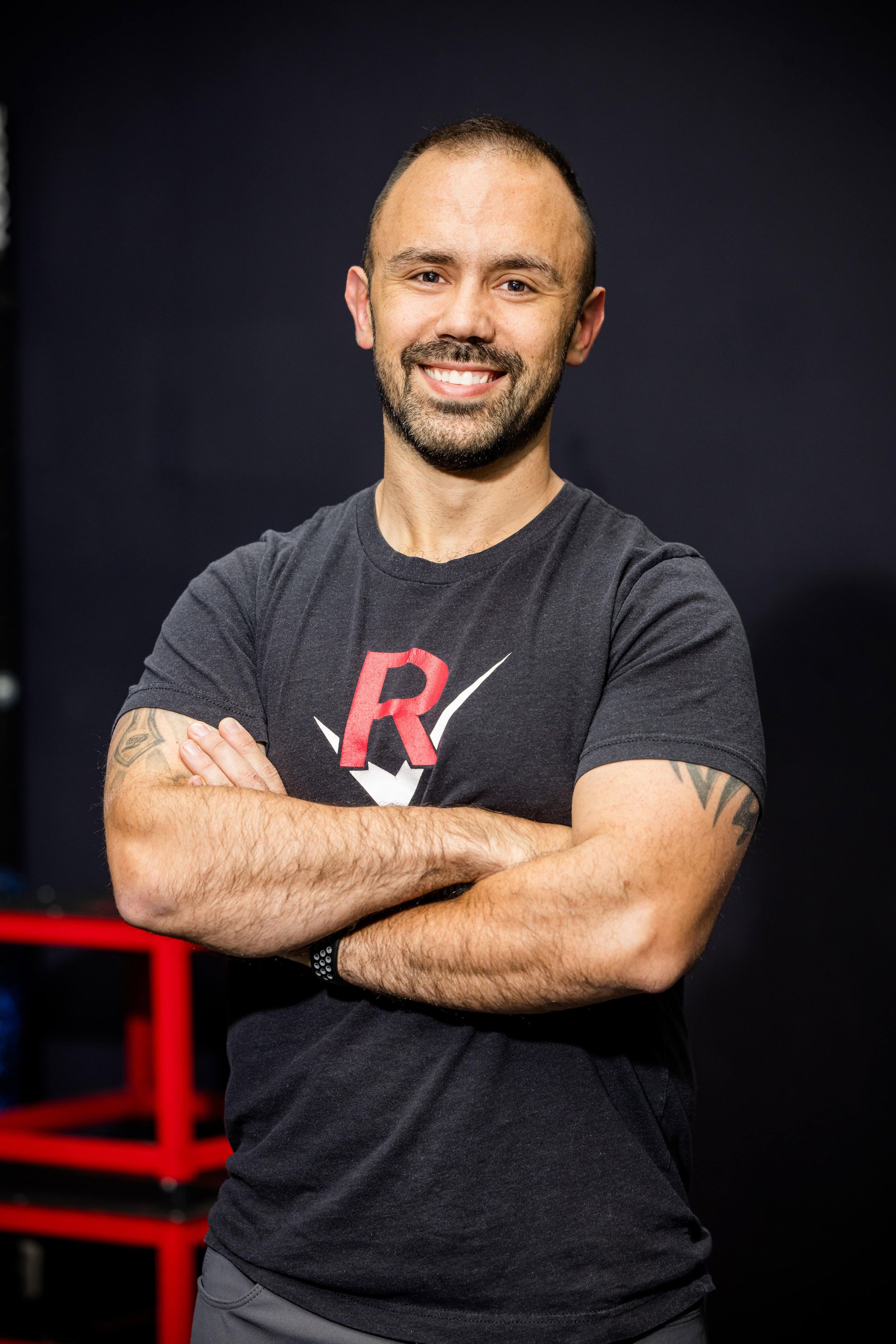 A man with a beard is standing in a gym with his arms crossed.
