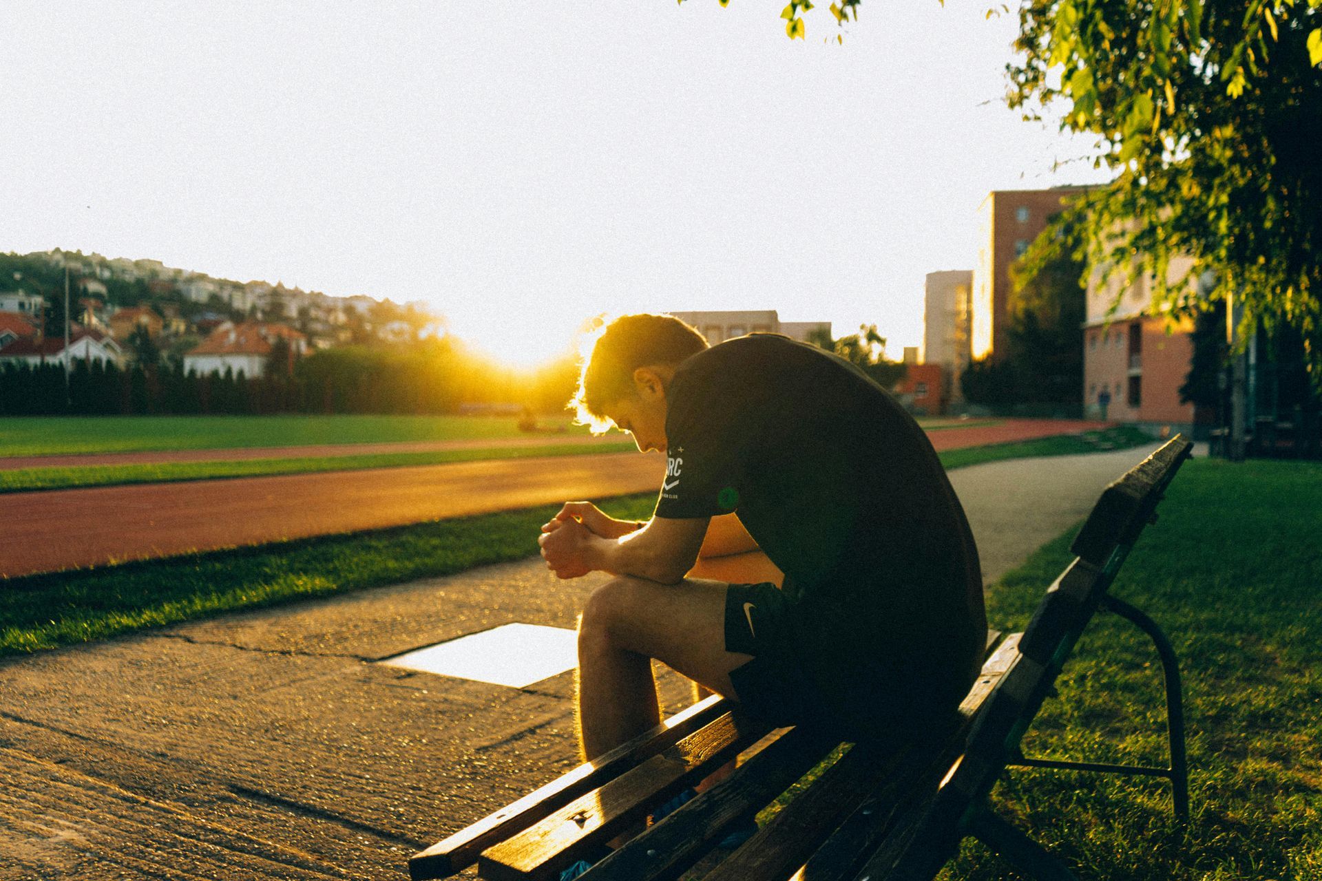 A man is sitting on a park bench with his head down.